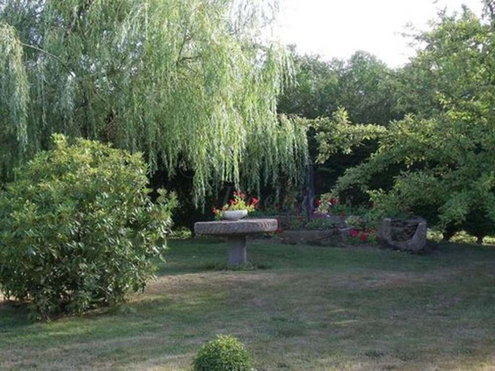 Garden with willow tree and stone table at Le Mont Rôti in Normandy